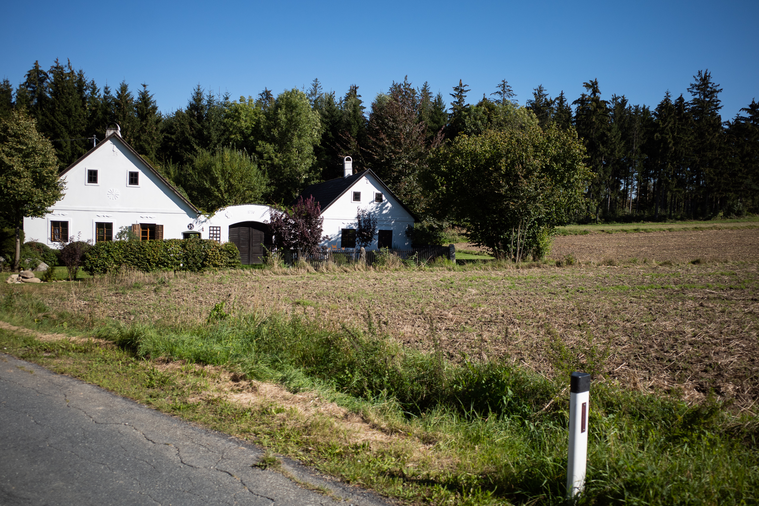 Weiß getünchte Höfe am Waldrand, davor das abgeerntete Feld